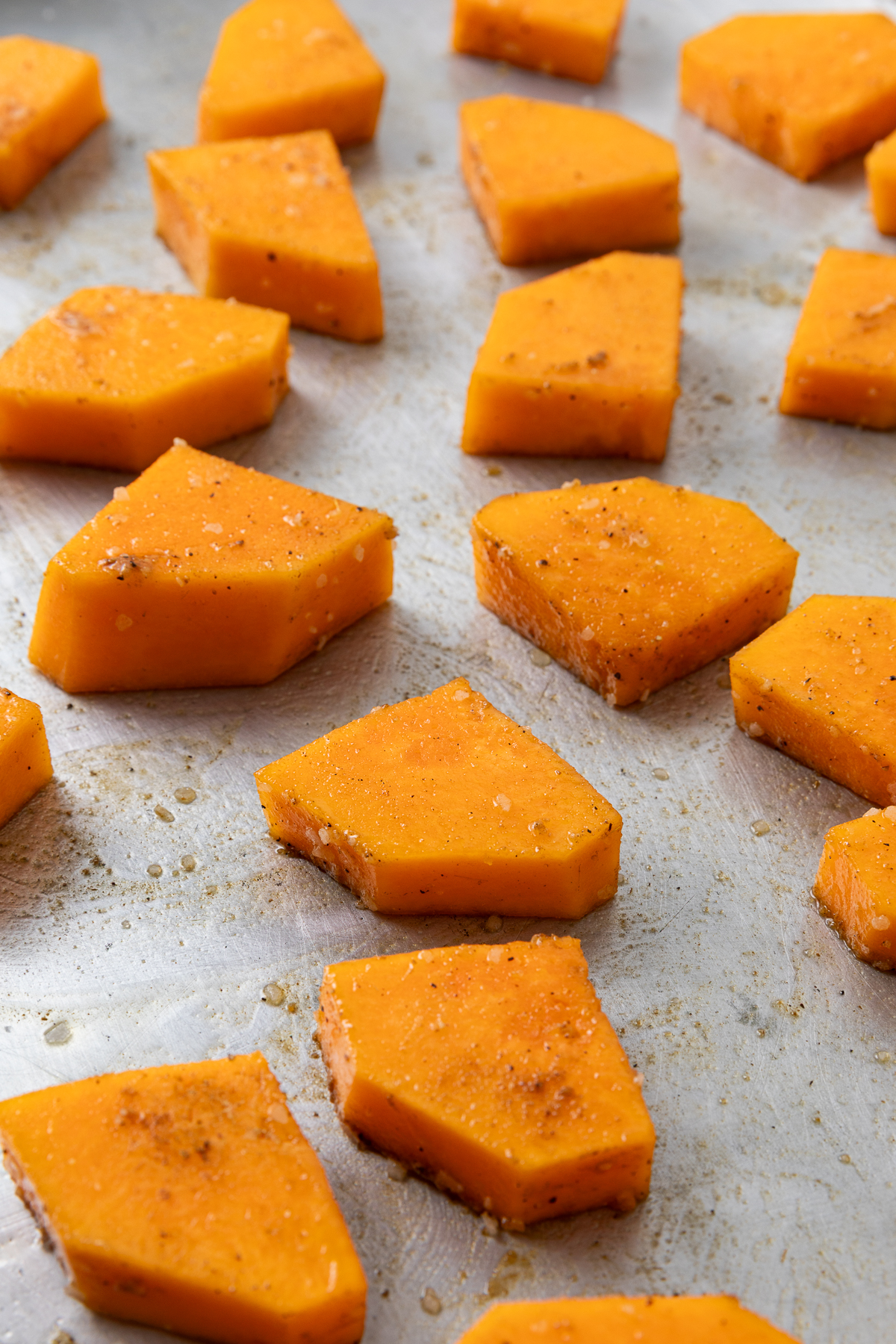 Cut pieces of butternut squash seasoned on a baking sheet.