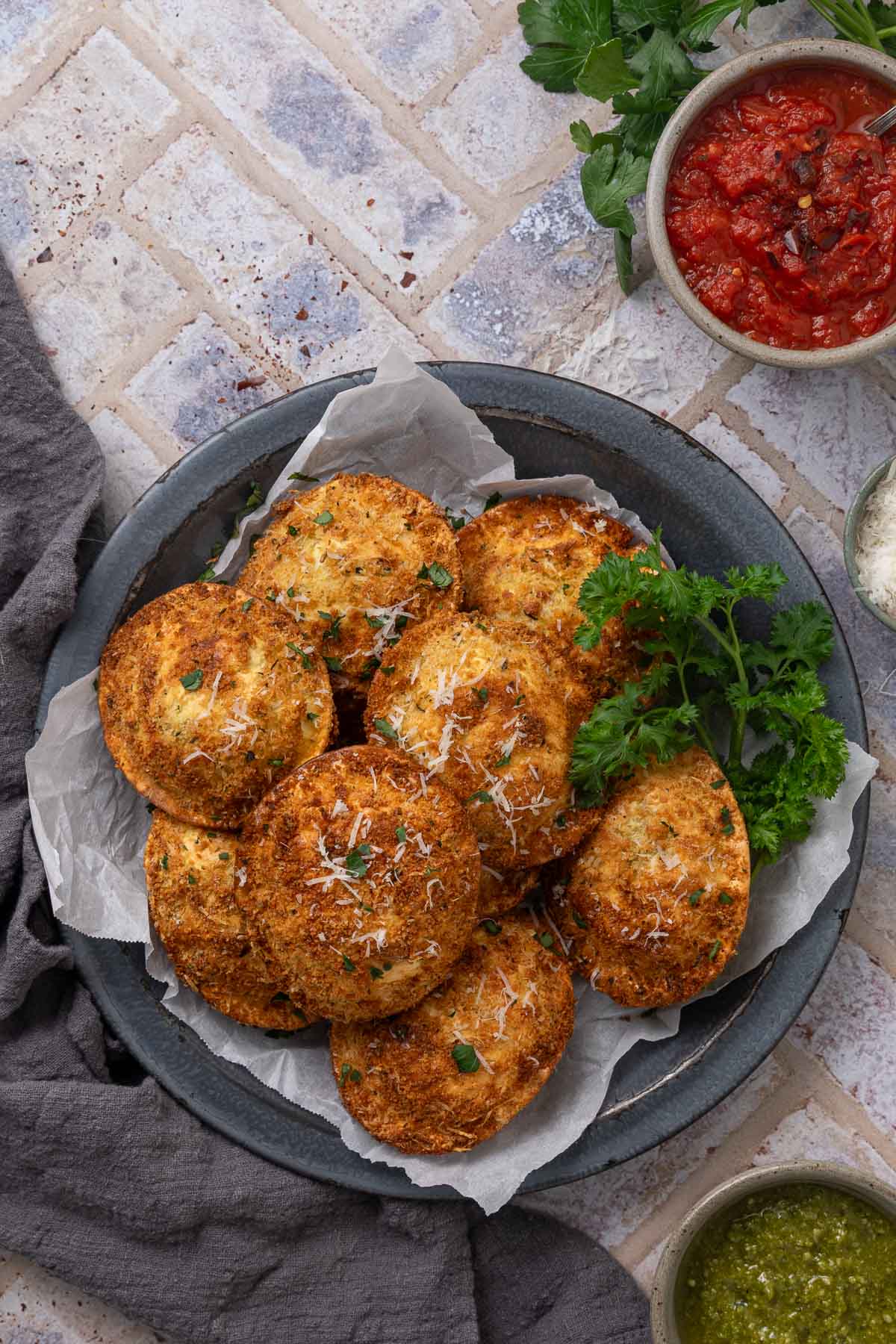 A pile of air fryer fried ravioli on a plate garnished with grated parmesan cheese and parsley. 