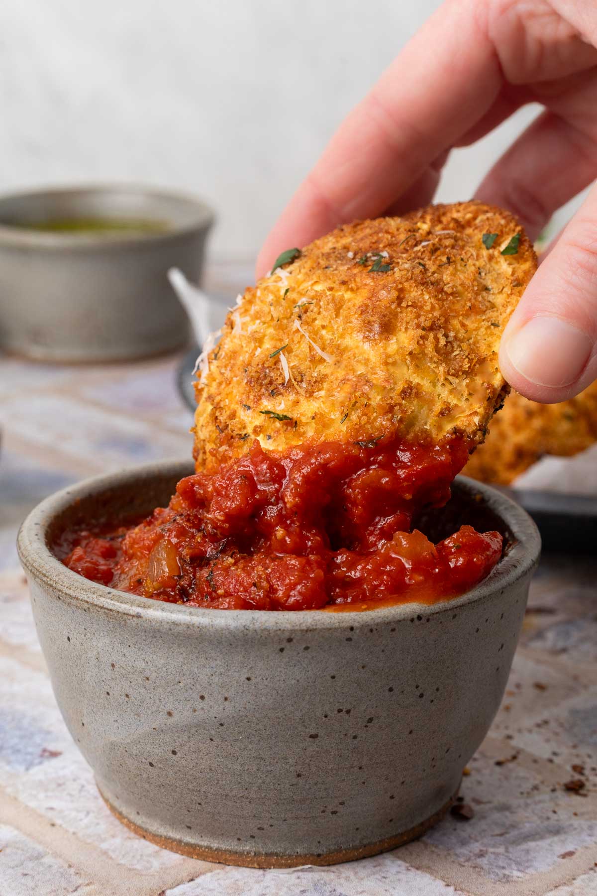 An air fried ravioli being dipped into a small bowl of homemade marinara.