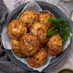 A pile of air fryer fried ravioli on a plate garnished with grated parmesan cheese and parsley.