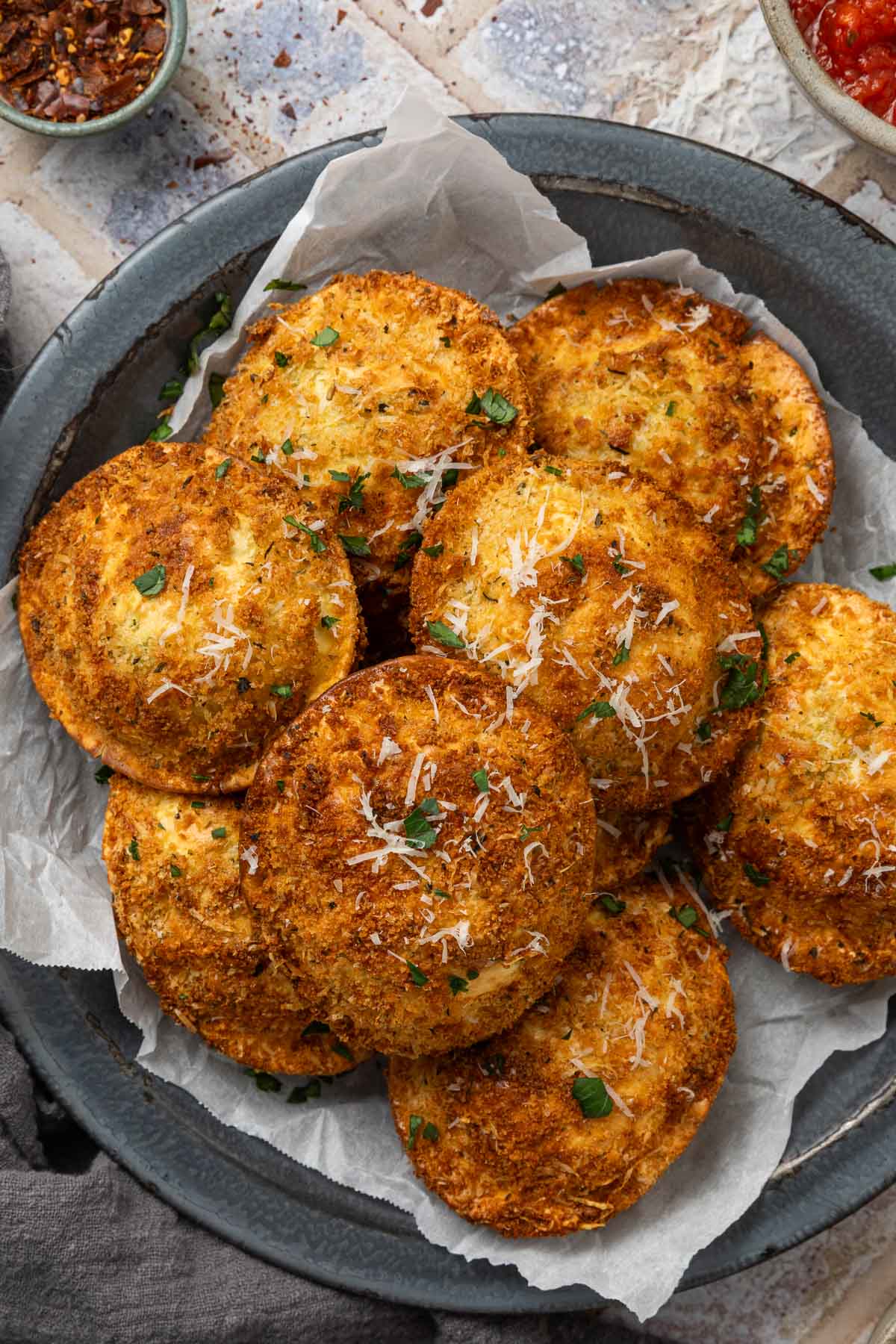 A pile of air fryer fried ravioli on a plate garnished with grated parmesan cheese and parsley.