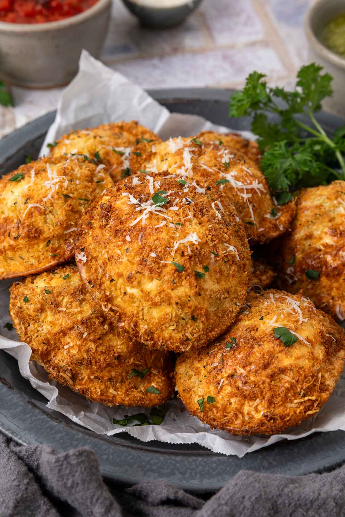 A pile of air fryer fried ravioli on a plate garnished with grated parmesan cheese and parsley.