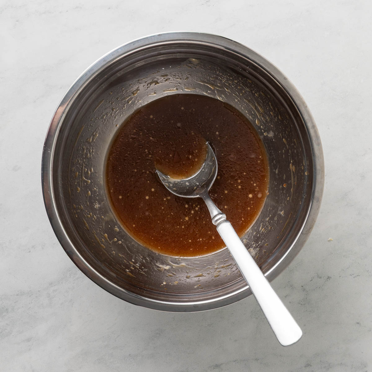 Sticky honey garlic sauce in a bowl with a spoon in it.