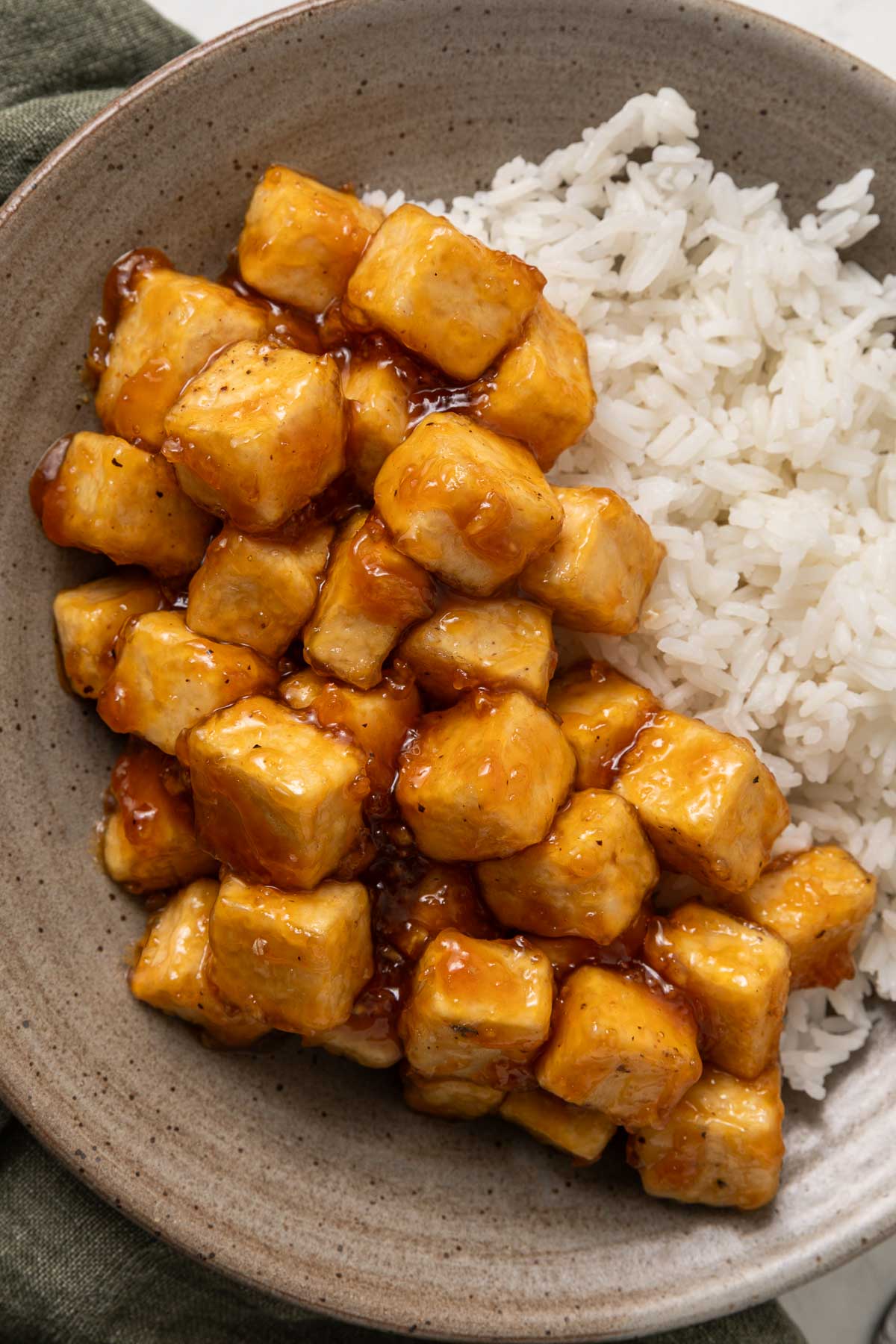 Sticky honey garlic tofu on a plate next to white rice.