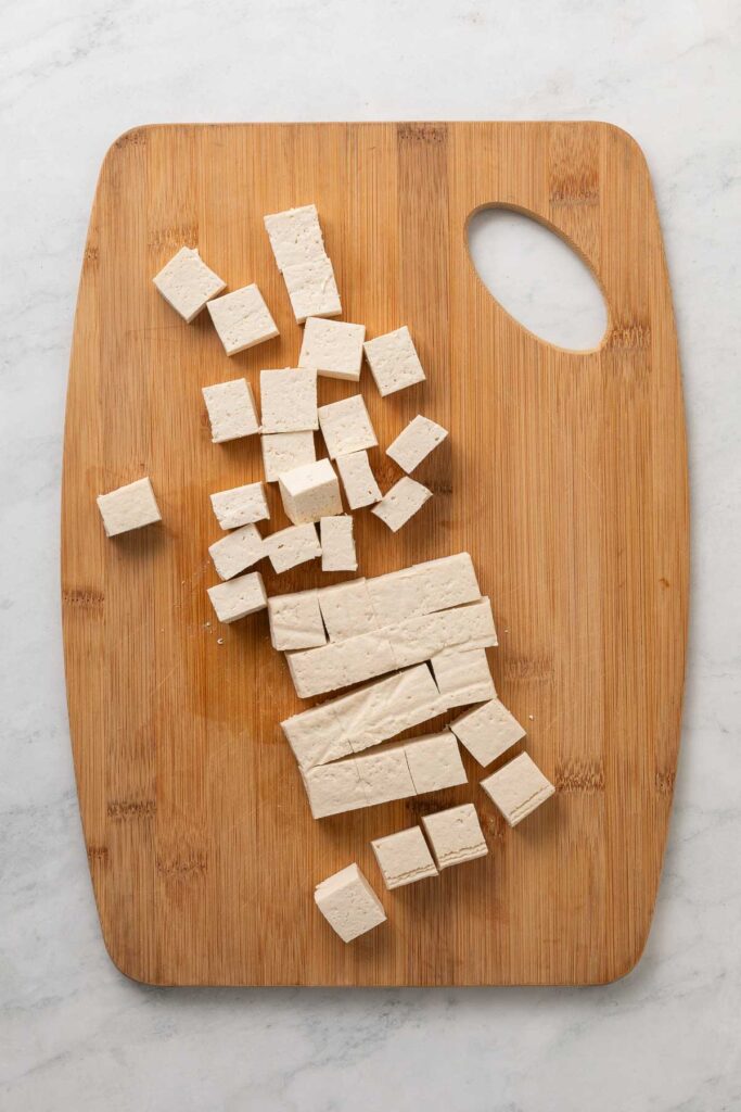 Tofu cut into cubes on a cutting board.