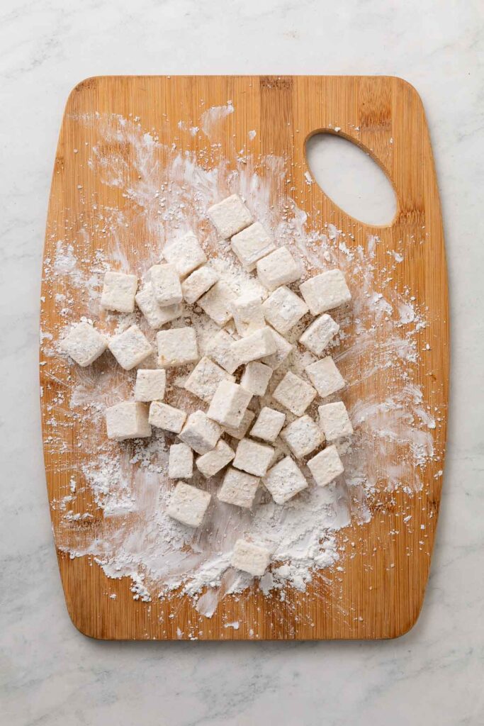 Cubes of tofu coated in corn starch on a cutting board.