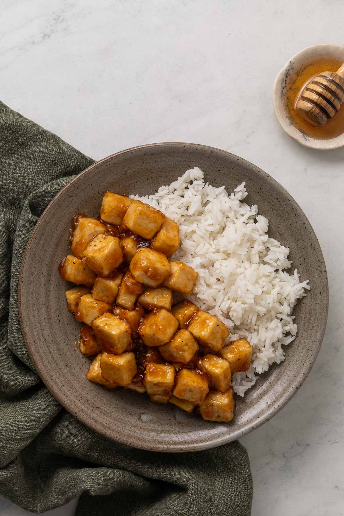 Sticky honey garlic tofu on a plate next to white rice.