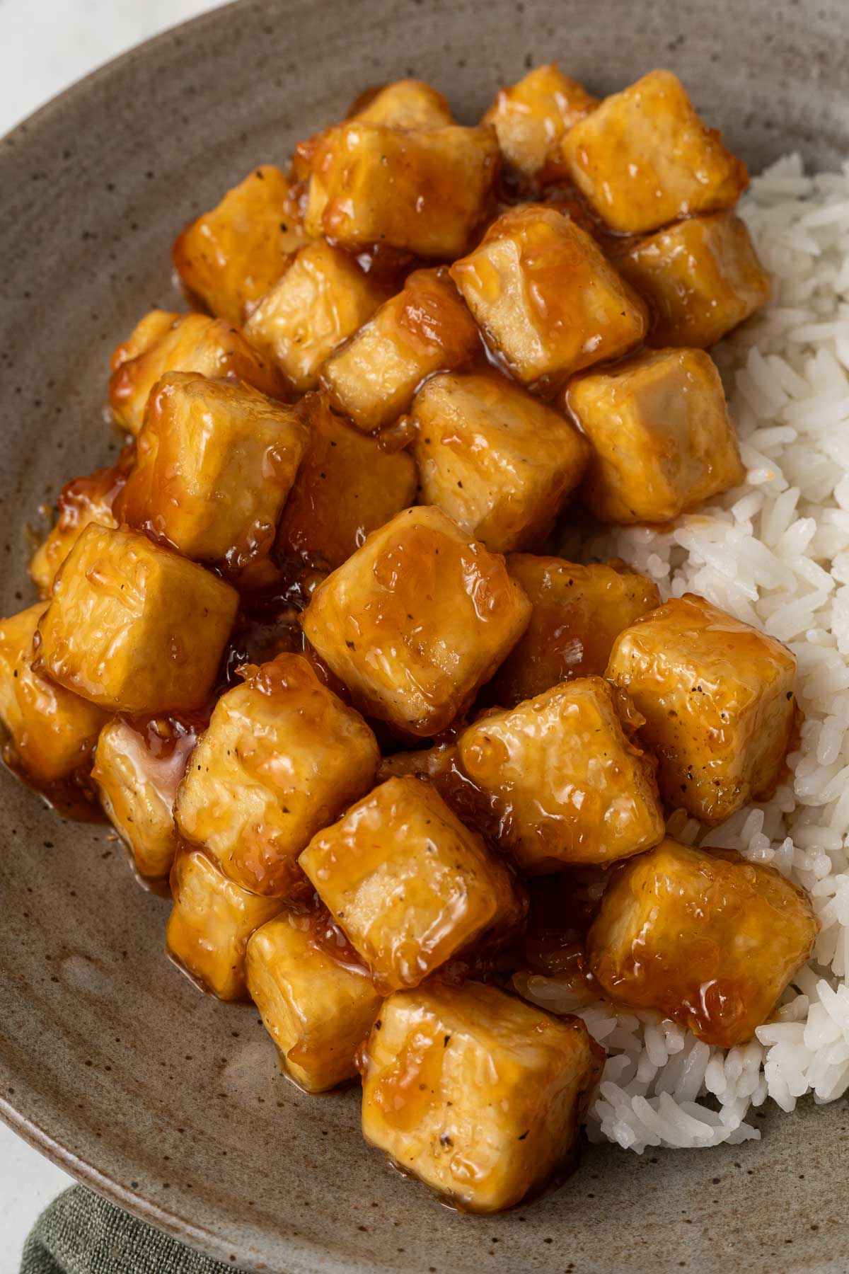Sticky honey garlic tofu on a plate next to white rice.