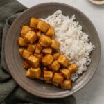 Sticky honey garlic tofu on a plate next to white rice.