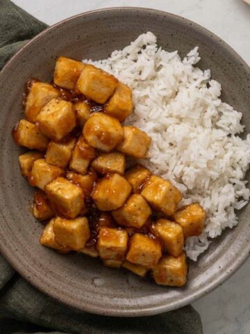Sticky honey garlic tofu on a plate next to white rice.