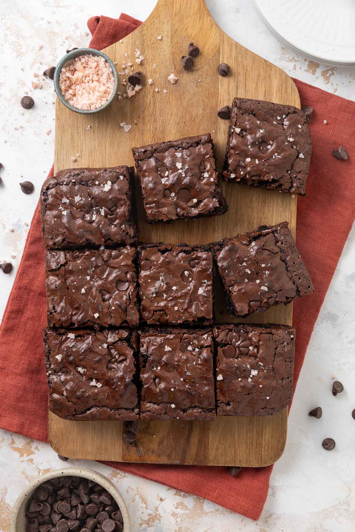 Chewy molasses brownies sliced on a cutting board next to a small bowl of flaky salt.
