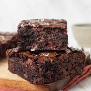 Two slices of chewy molasses brownies stacked on top of each other on a cutting board.