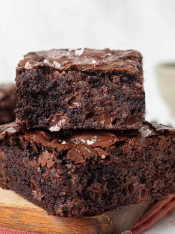 Two slices of chewy molasses brownies stacked on top of each other on a cutting board.