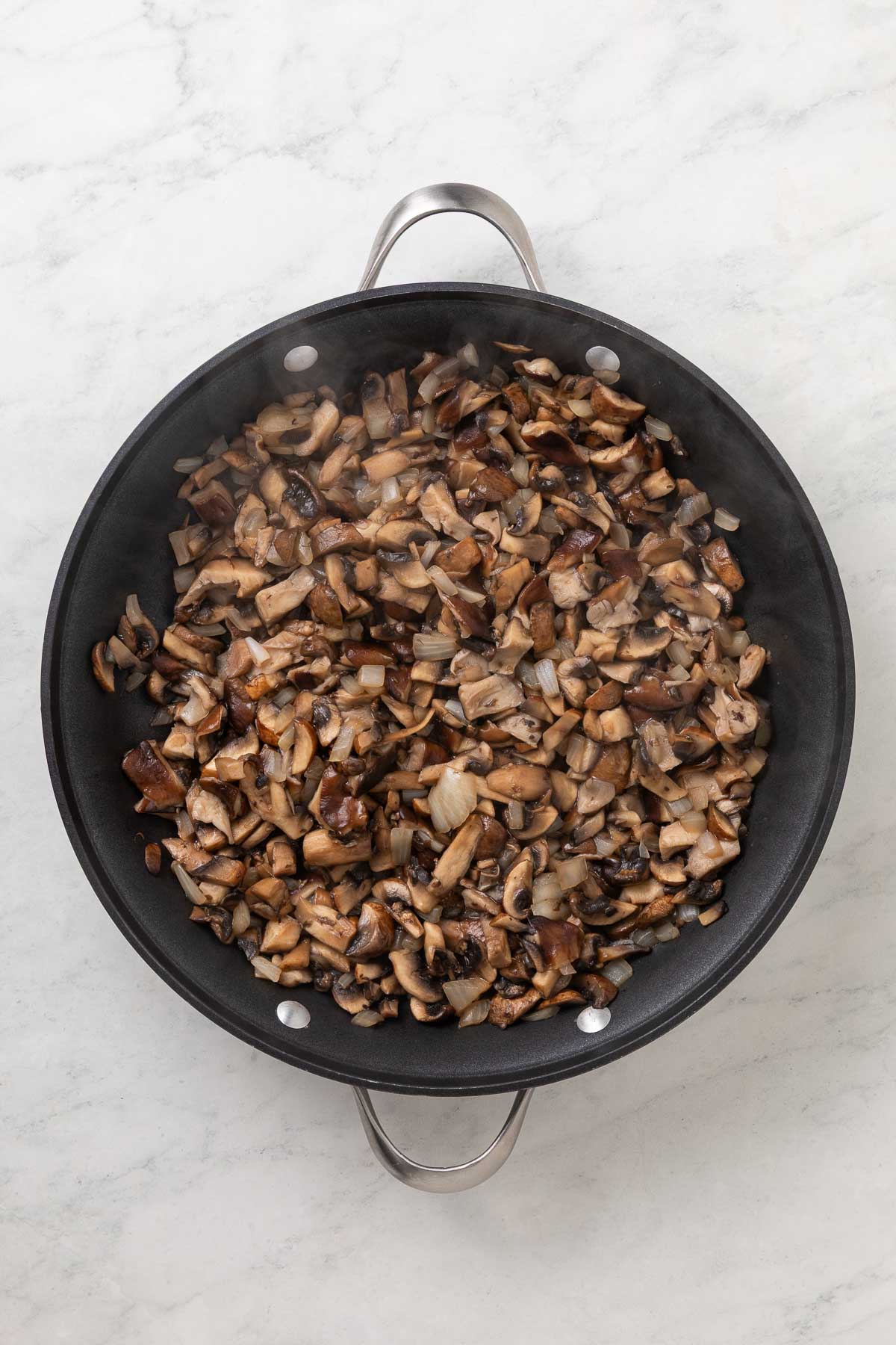 Onions and mushrooms cooking in a large pan.