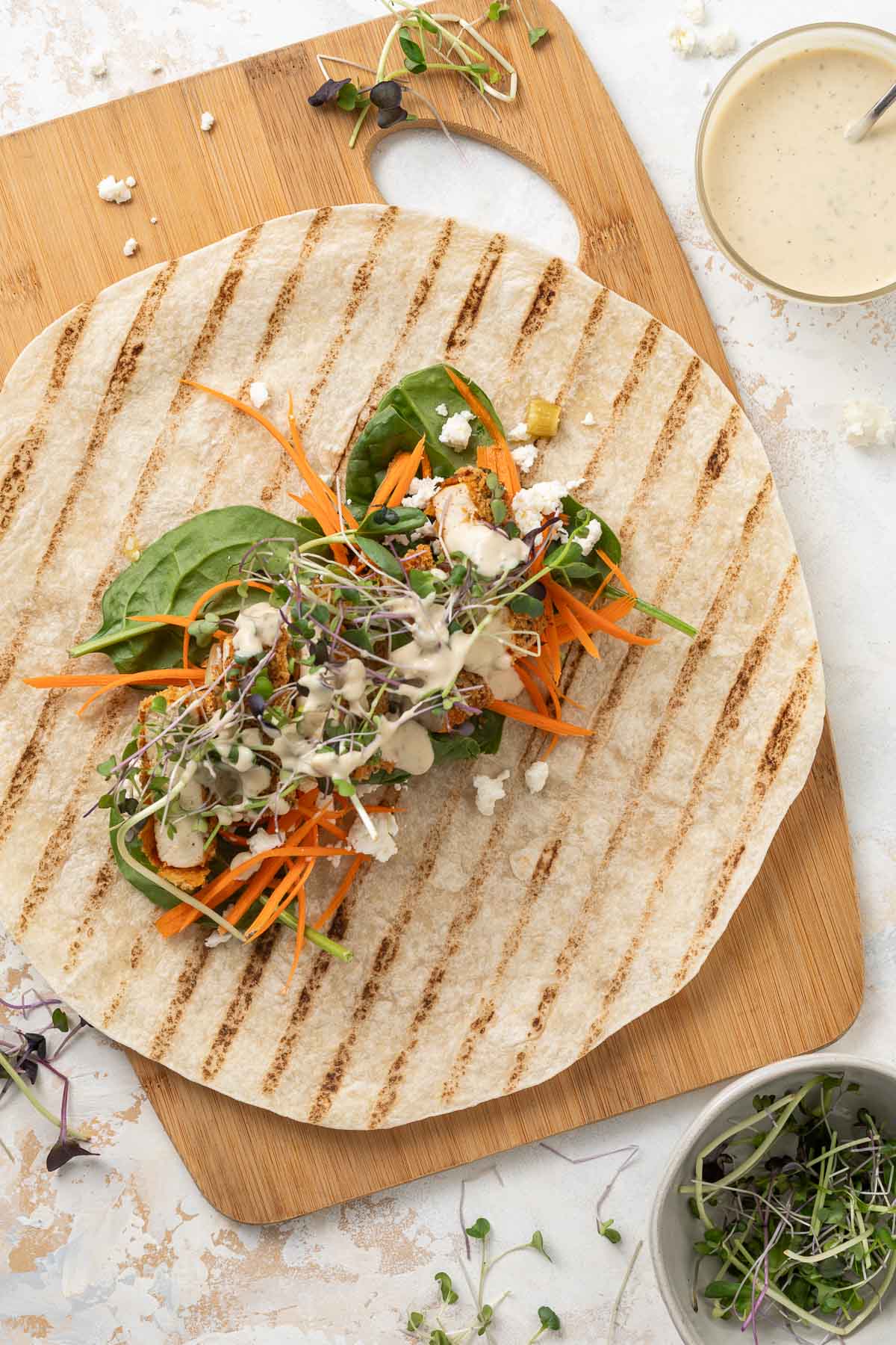 A crispy tofu wrap before it's wrapped, showing the ingredients laid out on a tortilla on a cutting board.
