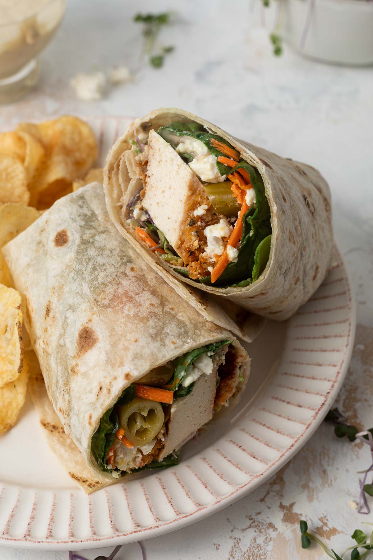 A crisp tofu wrap cut in half on a plate, with one half resting on top of the other.