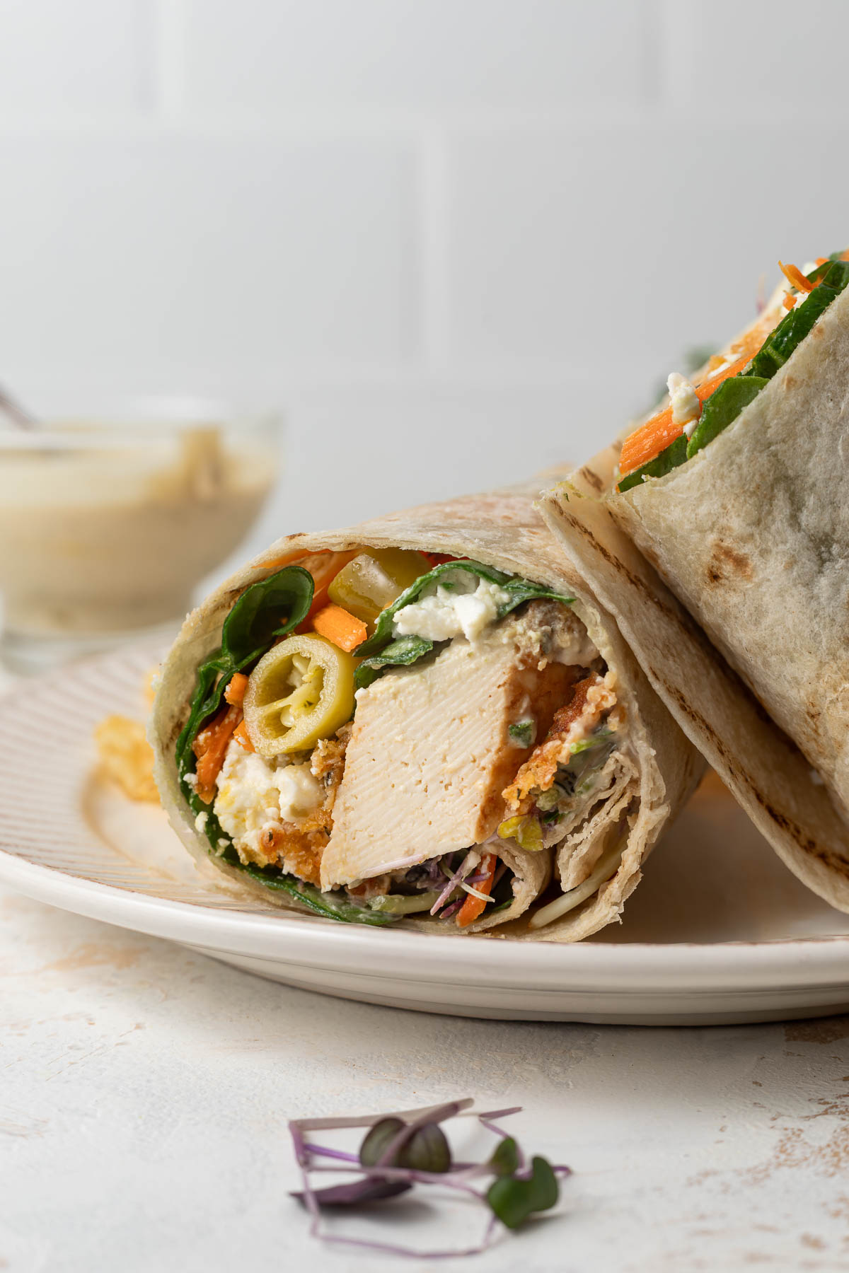 A crisp tofu wrap cut in half on a plate, with one half resting on top of the other.
