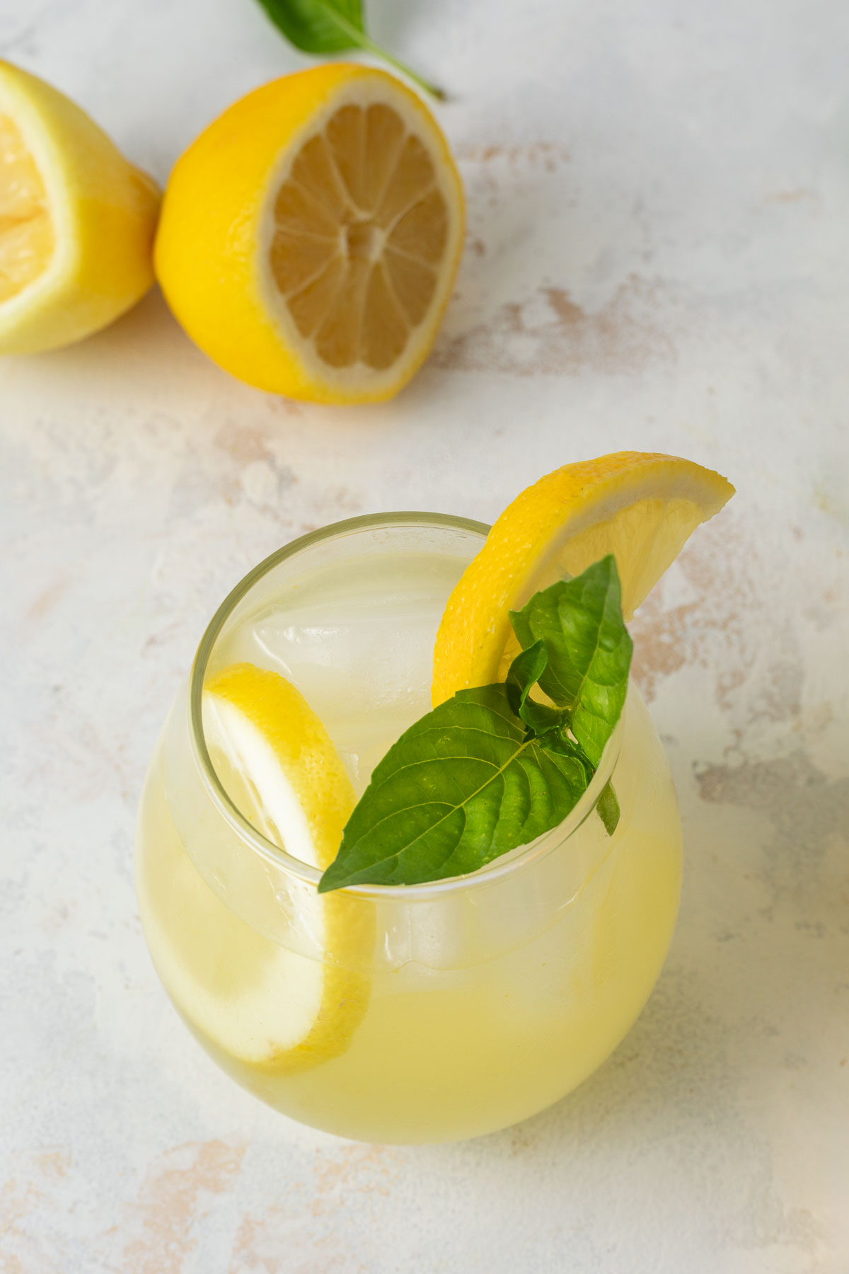 A glass of basil lemonade garnished with fresh lemon slices and fresh basil.
