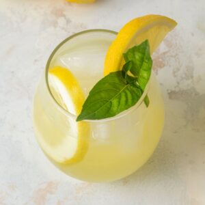 A glass of basil lemonade garnished with fresh lemon slices and fresh basil.