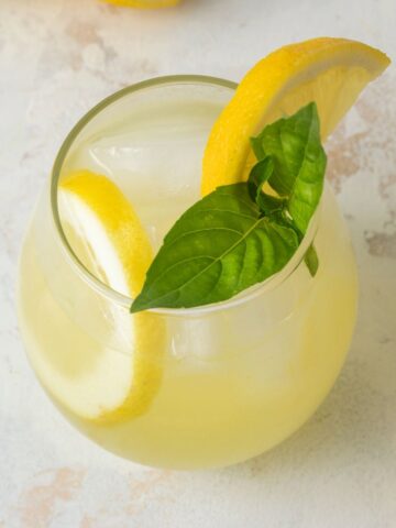 A glass of basil lemonade garnished with fresh lemon slices and fresh basil.