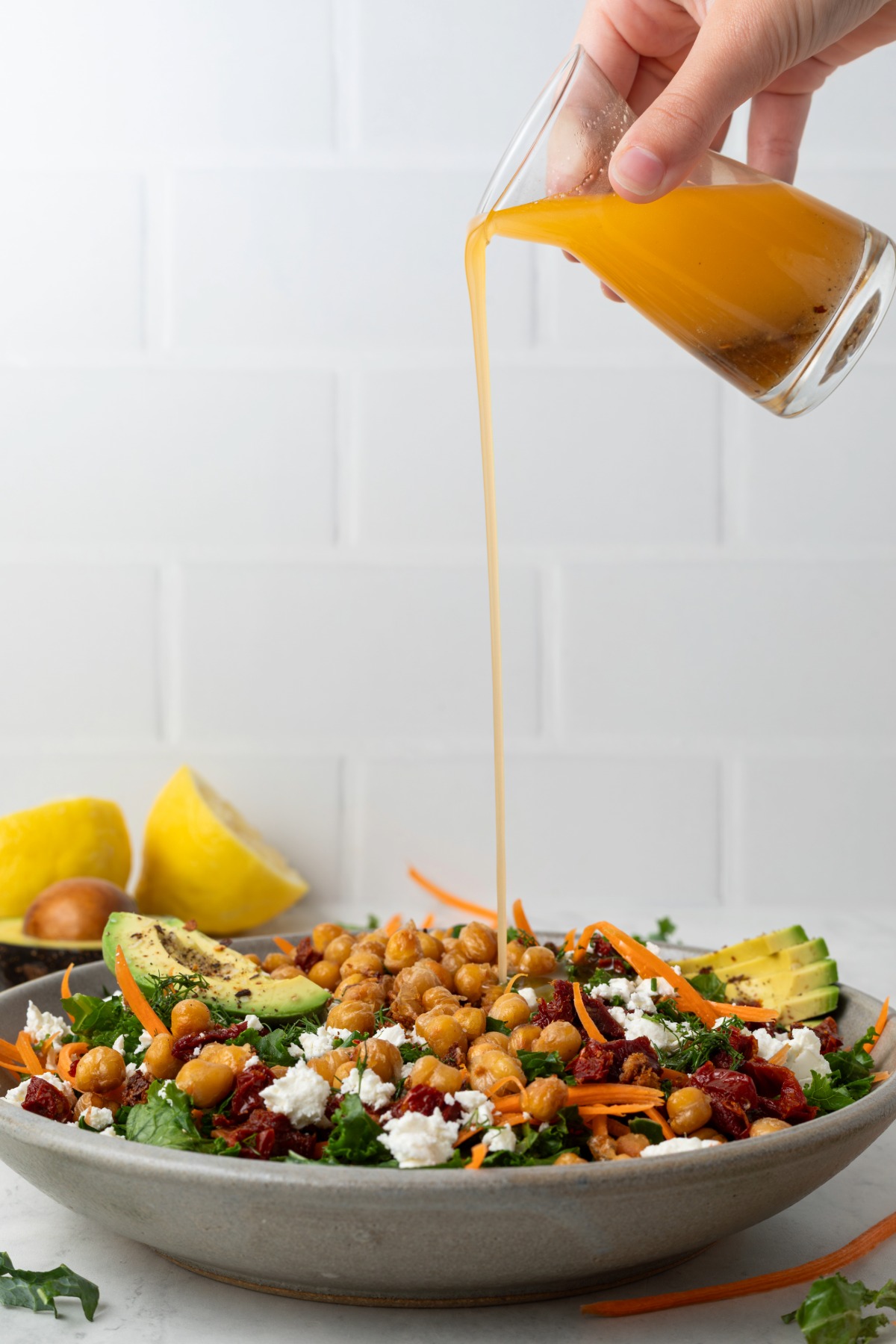 Sun dried tomato vinaigrette pouring on a bowl of chickpea and kale salad.