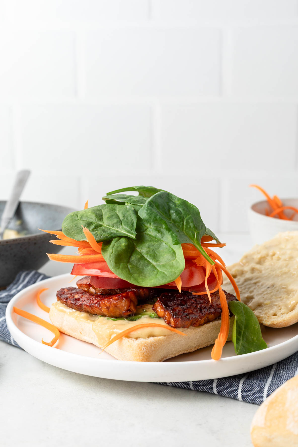 An open tempeh sandwich on a plate with the top of the bread resting off to the side.
