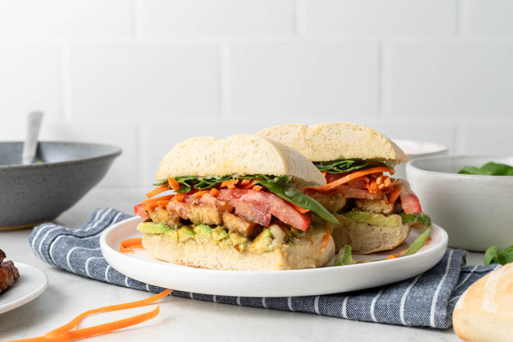 Side view of a tempeh sandwich cut in half on a white plate.