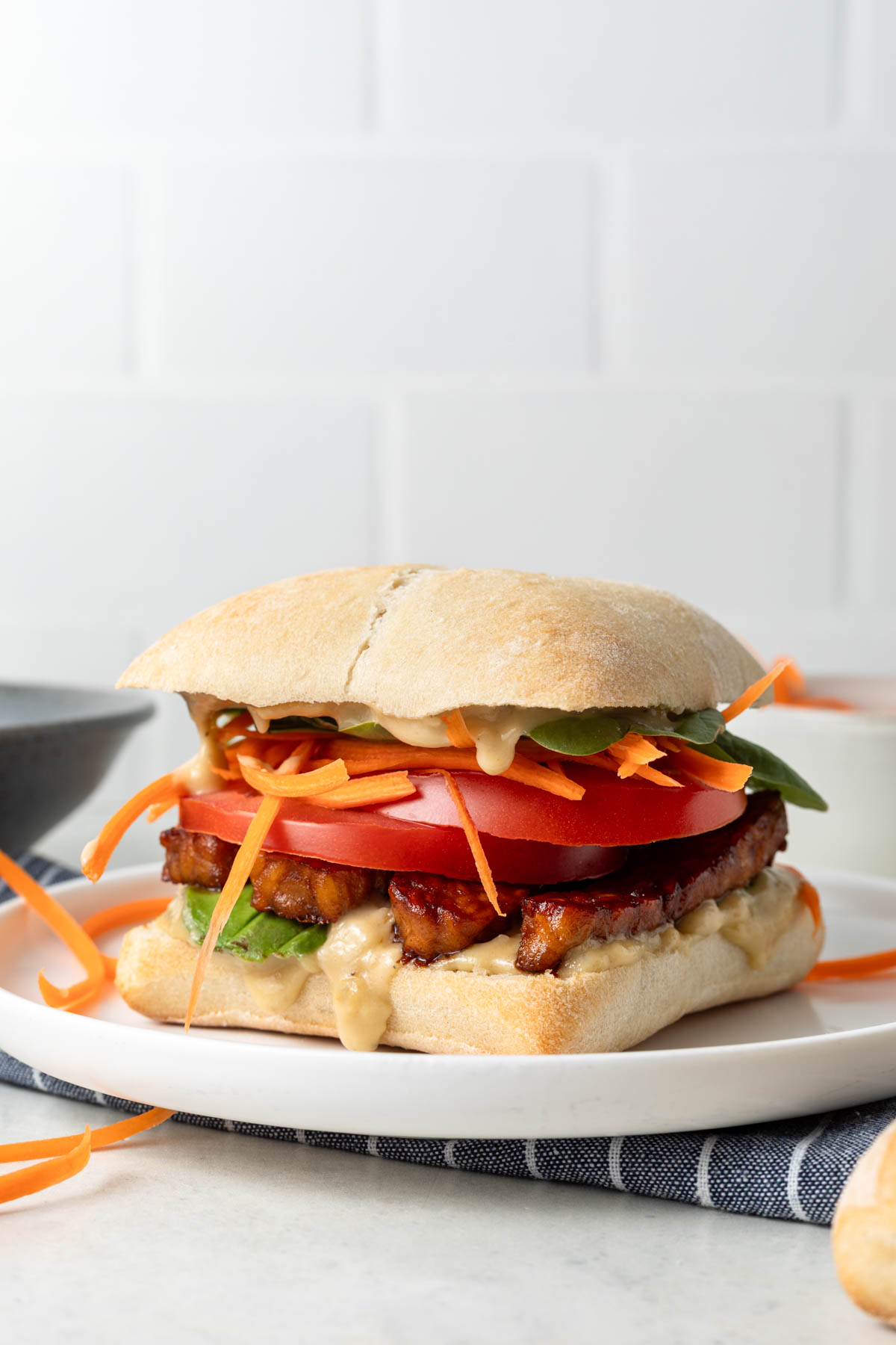 Side view of a tempeh sandwich on a white plate.